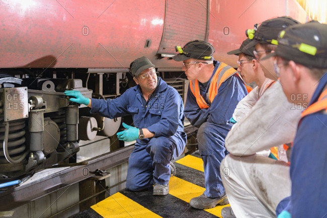 Engineer instructing apprentices with locomotive wheel lathe in train engineering factory