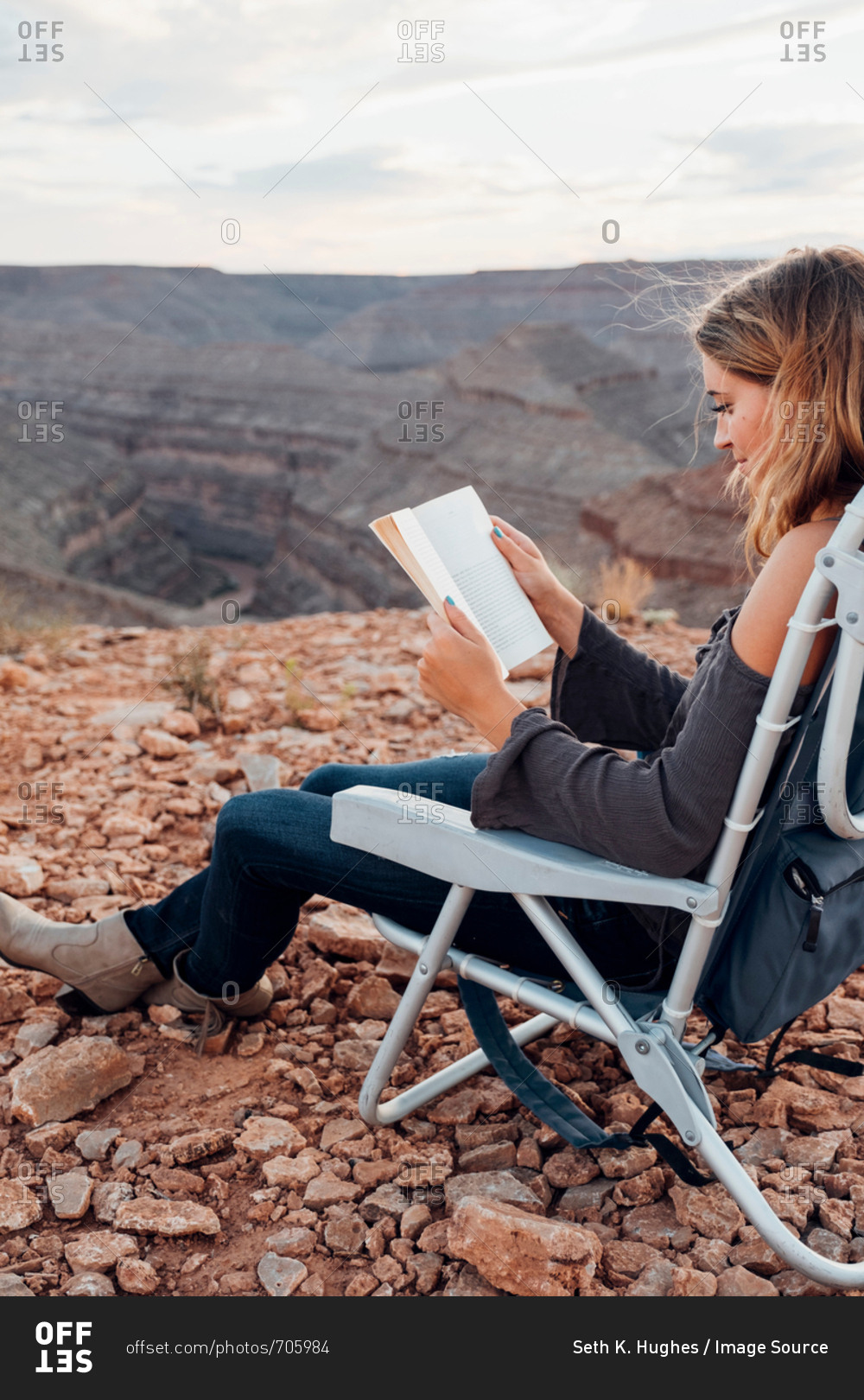Young woman in remote setting, sitting on camping chair, reading book, Mexican Hat, Utah, USA