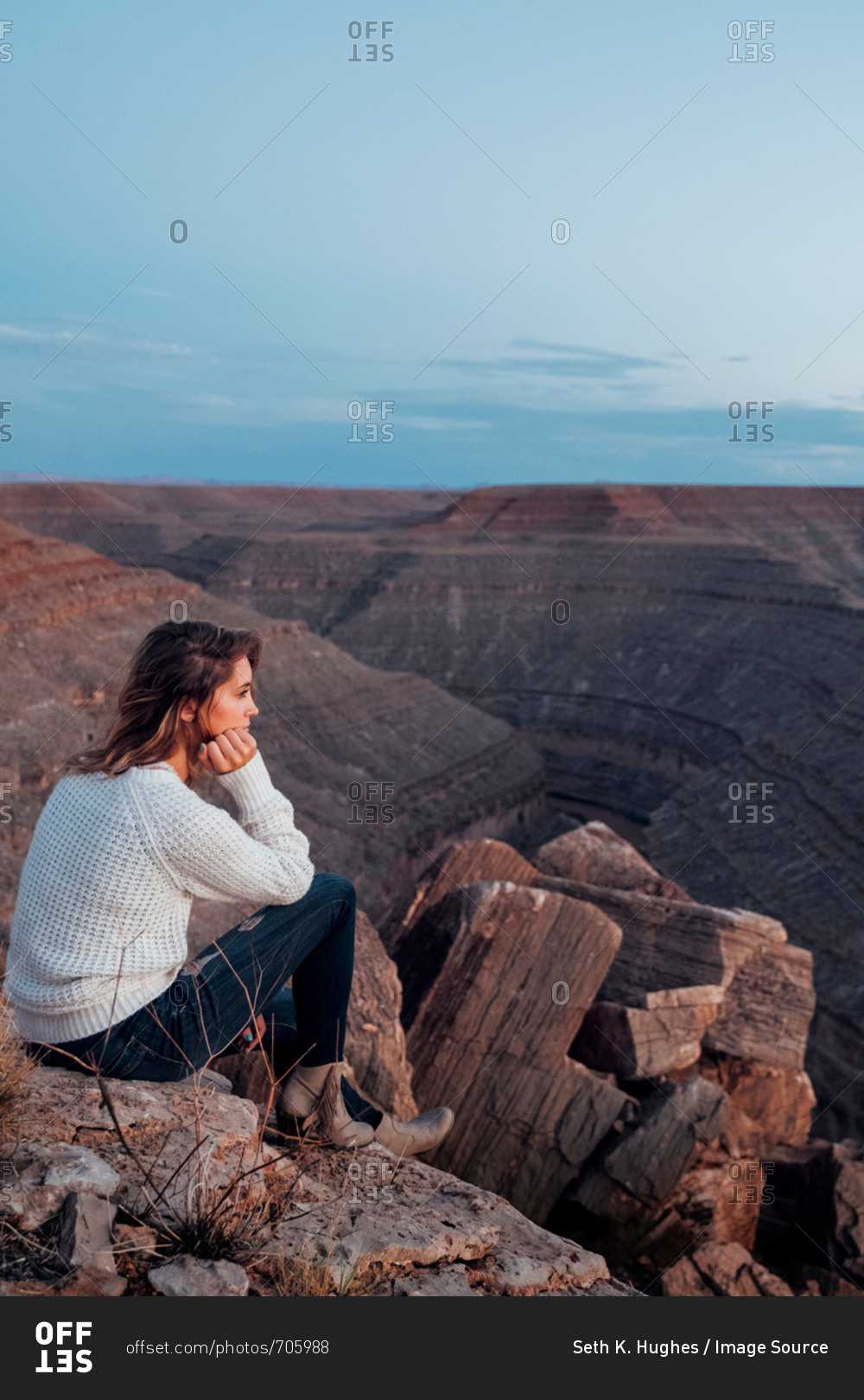 Young woman in remote setting, sitting on rocks, looking at view, Mexican Hat, Utah, USA