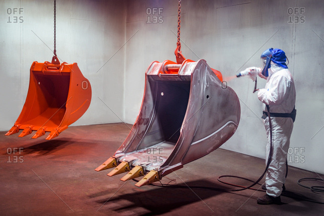 Spray painter painting digger buckets in spray booth in engineering factory