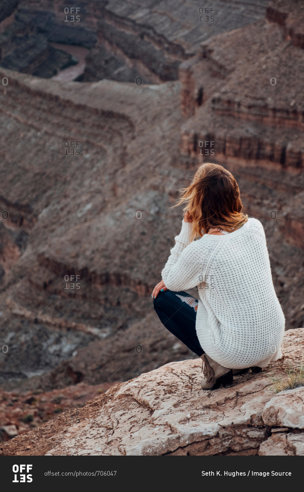 Young woman in remote setting, crouching on rocks, looking at view, rear view, Mexican Hat, Utah, USA