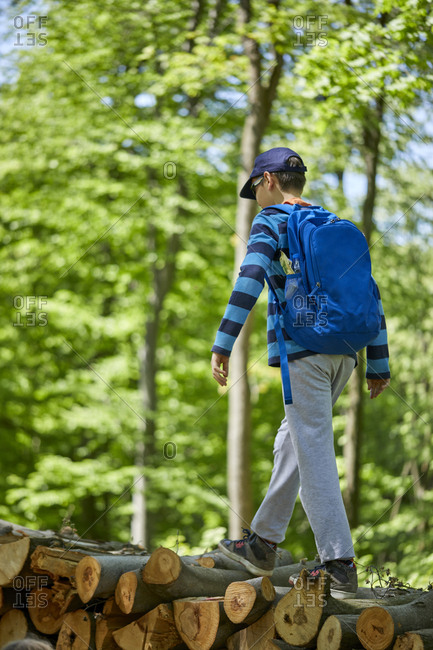 Boy with backpack balancing on logs in forest