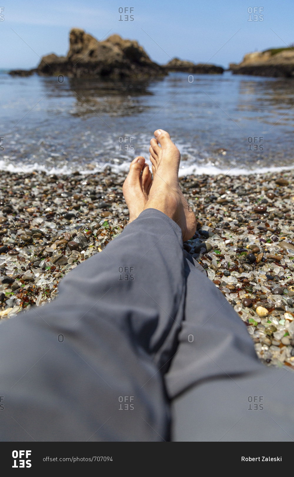 A man's bare feet resting on the coast at Glass Beach in Fort Bragg