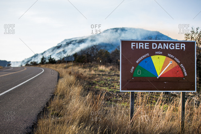 Fire danger sign with smoke from a wildfire in the mountains