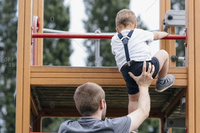 Toddler boy climbing up jungle gym with dad
