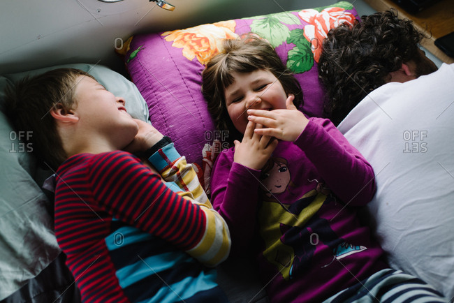 Two kids lying beside father in camper laughing