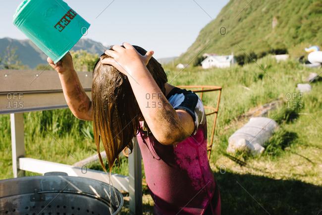 Little girl dumping a bucket of water over her muddy self