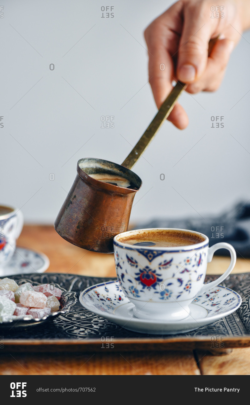 A woman pouring Turkish coffee into a Turkish coffee cup from a copper Turkish coffee pot