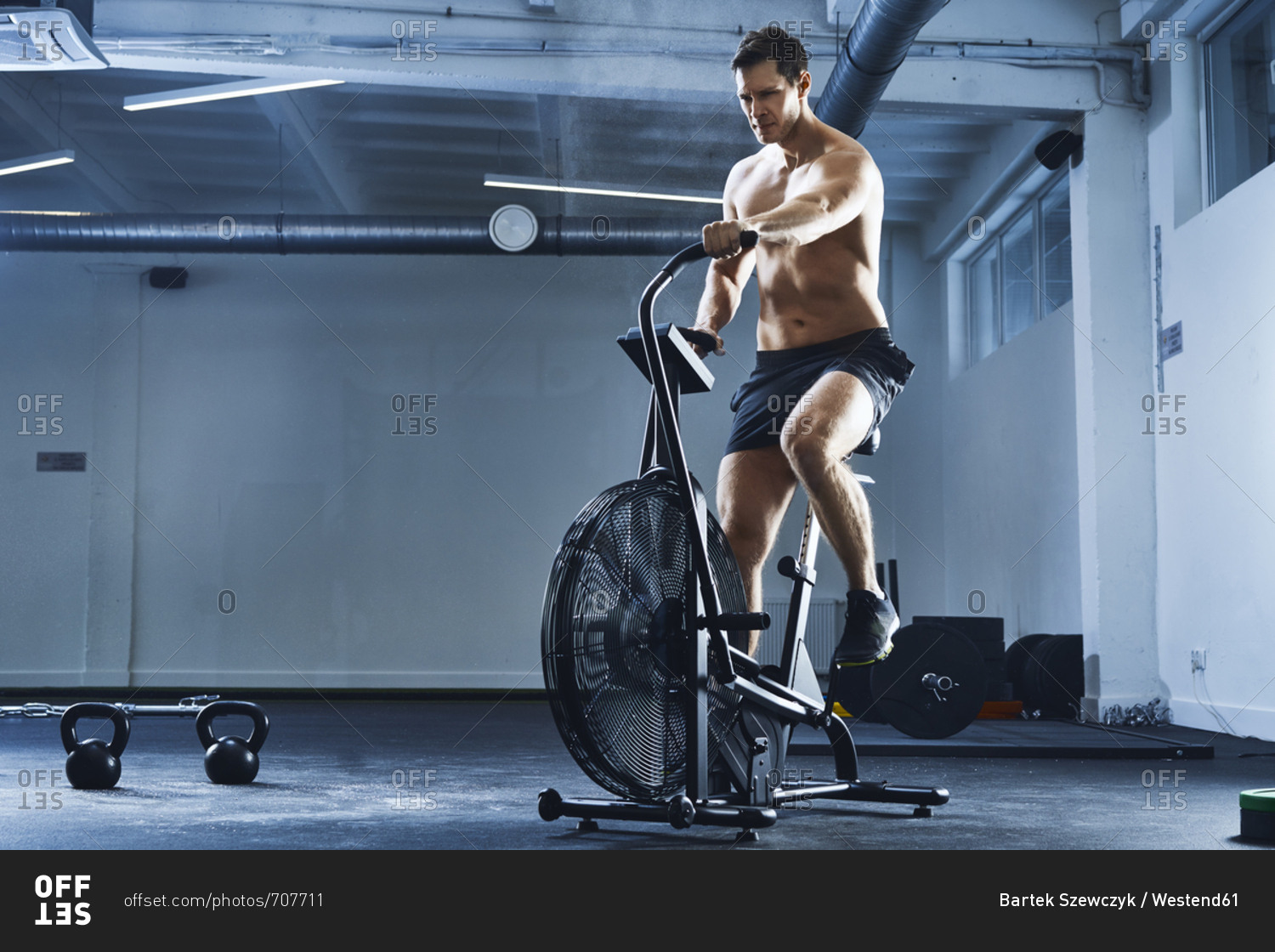 Athletic man doing HIIT workout on air bike at gym