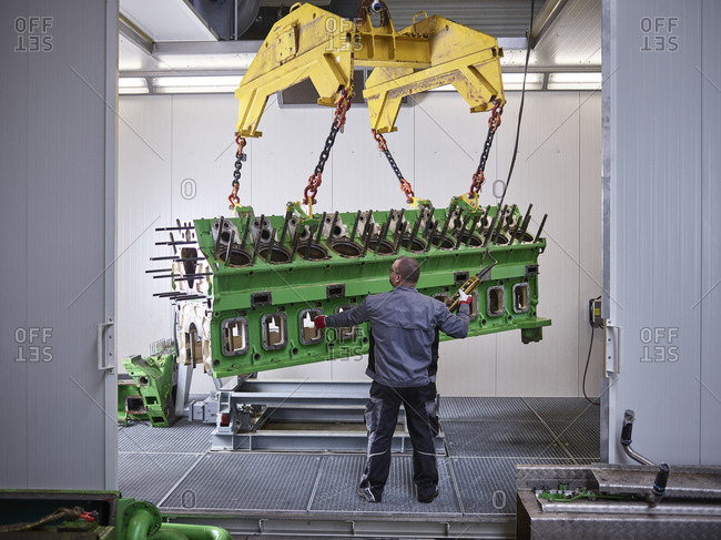 Worker in factory lifting engine block with crane
