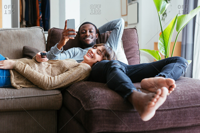 Happy Mixed Race Couple Relax On Couch In Living Room Watch Movie