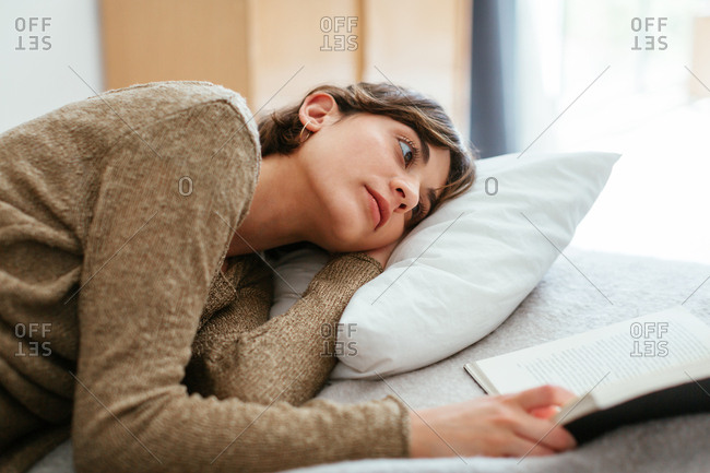 Young woman relaxing on bed reading a book