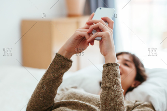 Young woman chatting on phone lying on bed