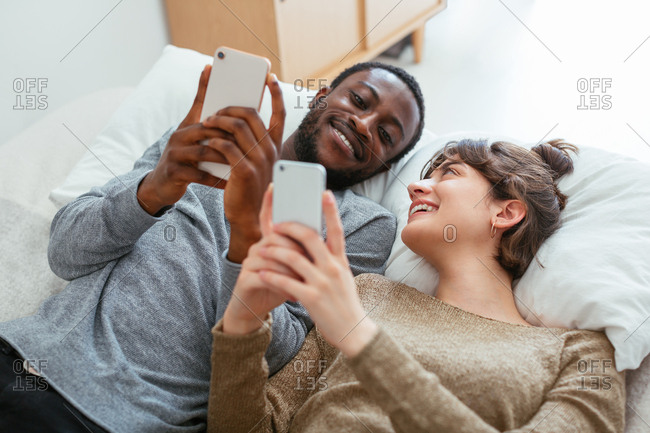 Young couple using their phones lying on bed