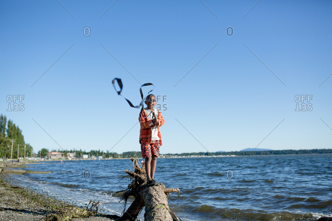 Boy standing on a log waving a streamer on a stick on a breezy day at the beach