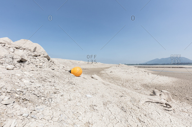 Yellow buoy lying next to tree stump on bed of arid dirt of lake Forggensee in Germany