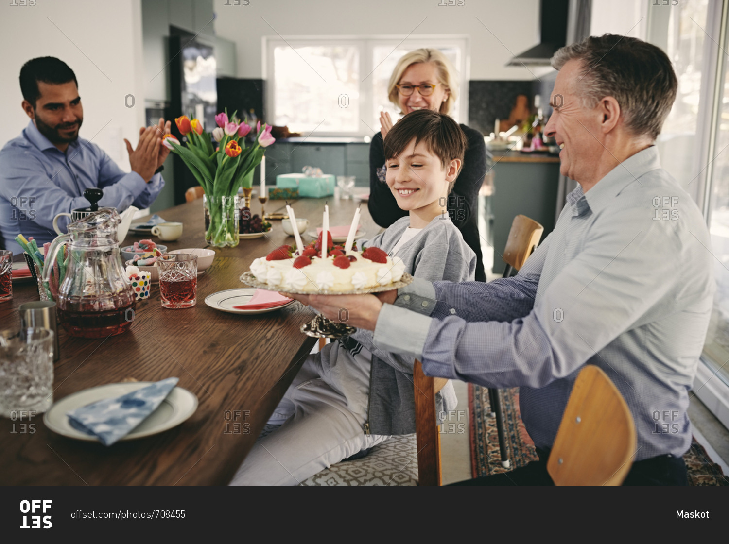 Smiling boy with grandparents and father with birthday cake at table
