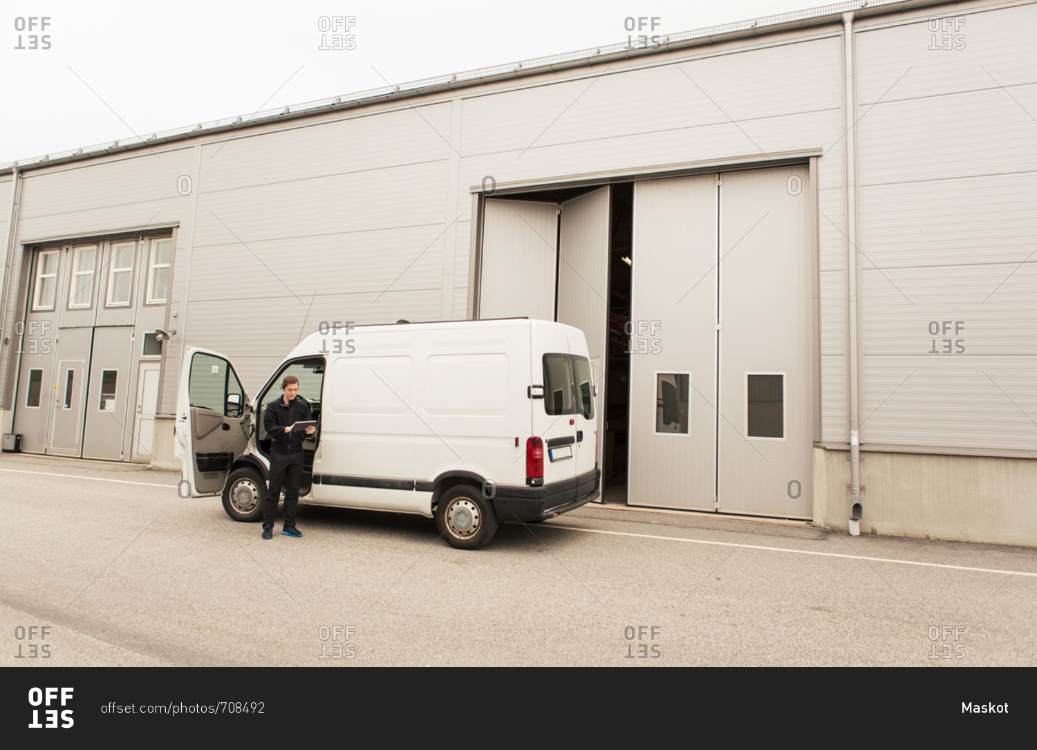 Manual worker standing by delivery van on road by industry