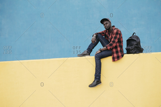 African man sitting on a yellow wall with blue background
