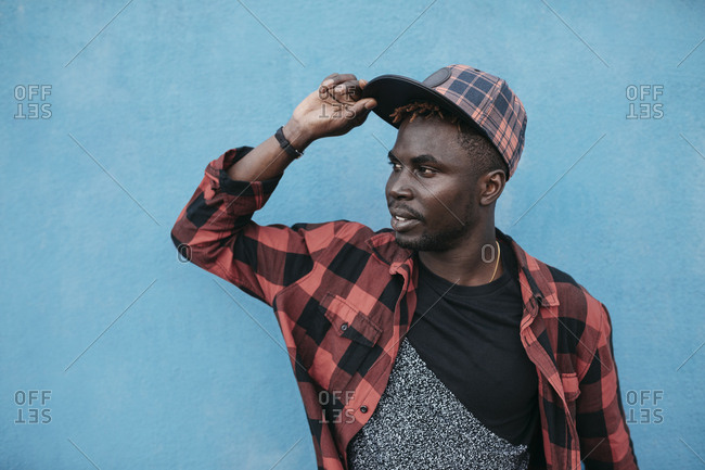 Handsome black man with cap on a blue wall, wearing casual clothing
