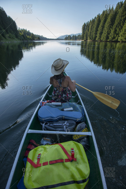 Adult woman canoeing down a river with all of her gear for overnight camping