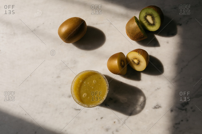 Top down view of kiwi fruits cut into halves and a glass of kiwi fruit juice