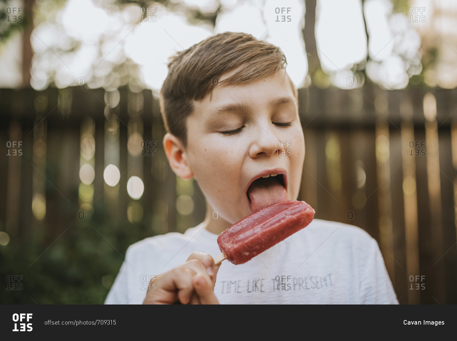 close-up-of-boy-licking-popsicle-at-backyard-during-summer-stock-photo