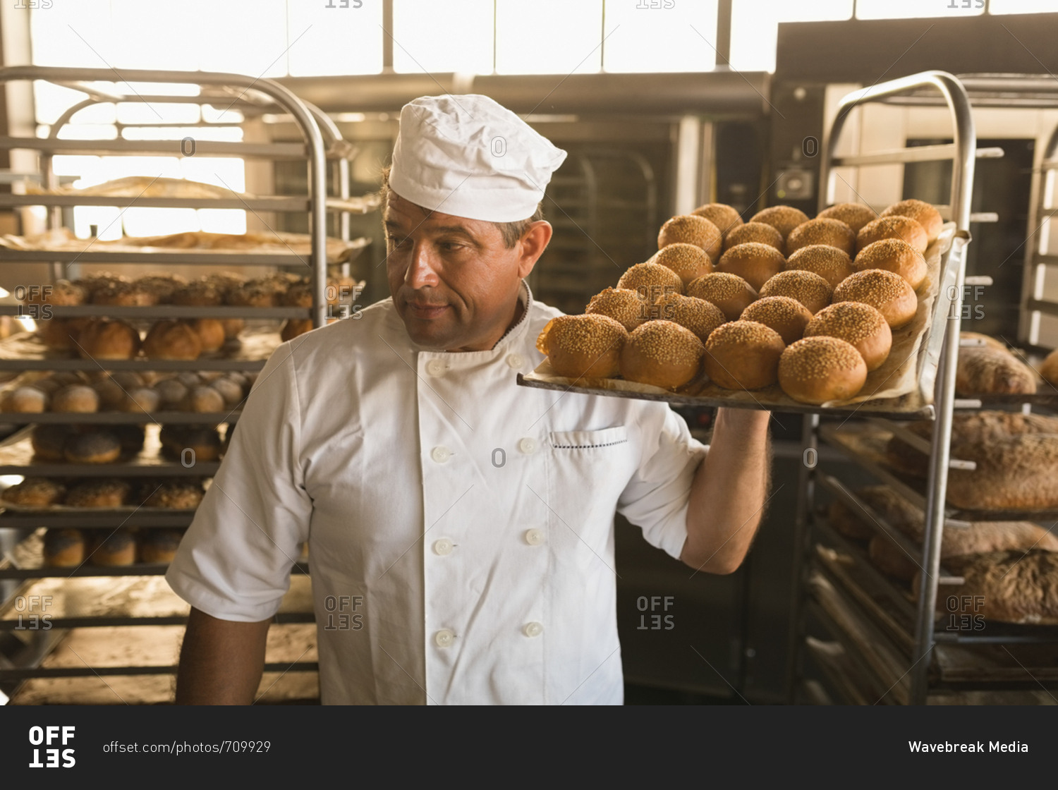 Male baker holding a tray of baked sweet foods in bakery shop