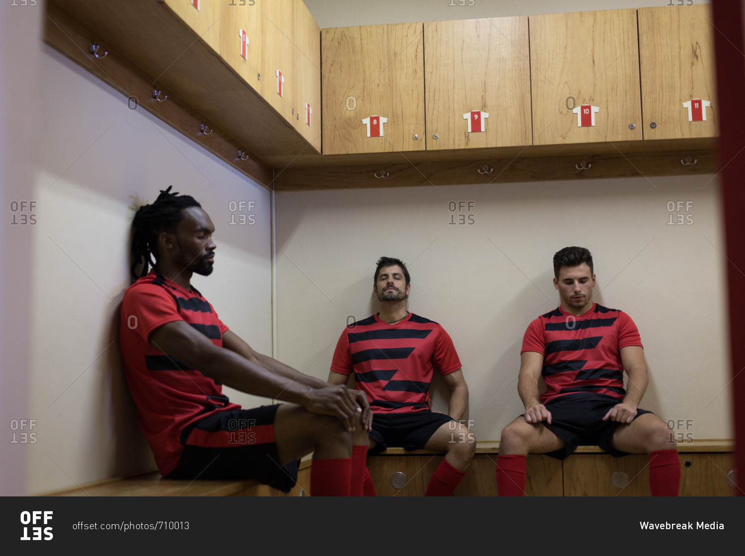 Football players relaxing on bench in dressing room