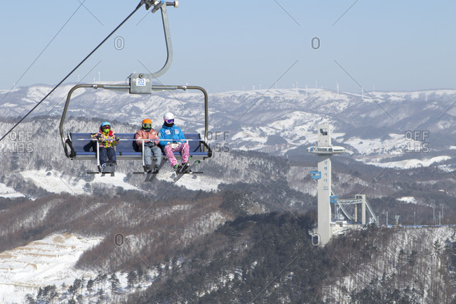 January 22, 2017: Colorful dressed skiers in a chair lift high above Alpensia resort in the Gangwon-do region of South Korea.  The Alpensia Resort is a ski resort and a tourist attraction. It is located on the territory of the township of Daegwallyeong-myeon, in the county of Pyeongchang, hosting the Winter Olympics in February 2018.  The ski resort is approximately 2.5 hours from Seoul or Incheon Airport by car, predominantly all motorway.   Alpensia has six slopes for skiing and snowboarding, with runs up to 1.4 km (0.87 mi) long, for beginners and advanced skiers, and an area reserved for snowboarders. While the resort is open year-round, the off-season turns the bottom of the slopes into a wild flower garden estimating 100,000-square meters.