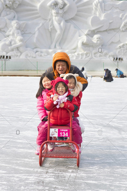 January 17, 2018: A Asian family on a special group sled at the Hwacheon Sancheoneo Ice Festival.     The Hwacheon Sancheoneo Ice Festival is a tradition for Korean people. Every year in January crowds gather at the frozen river to celebrate the cold and snow of winter. Main attraction is ice fishing. Young and old wait patiently over a small hole in the ice for a trout to bite. In tents they can let the fish grilled after which they are eaten. Among other activities are sledding and ice skating.    The nearby Pyeongchang region will host the Winter Olympics in February 2018.