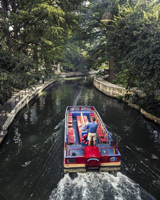 September 17, 2017: A man drives a water taxi along the San Antonio river walk on a sunny late summer day. The riverwalk is covered with a canopy of trees and makes for a nice peaceful place to walk.