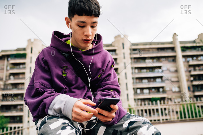 Young Asian man using smart phone and listening to music outdoors