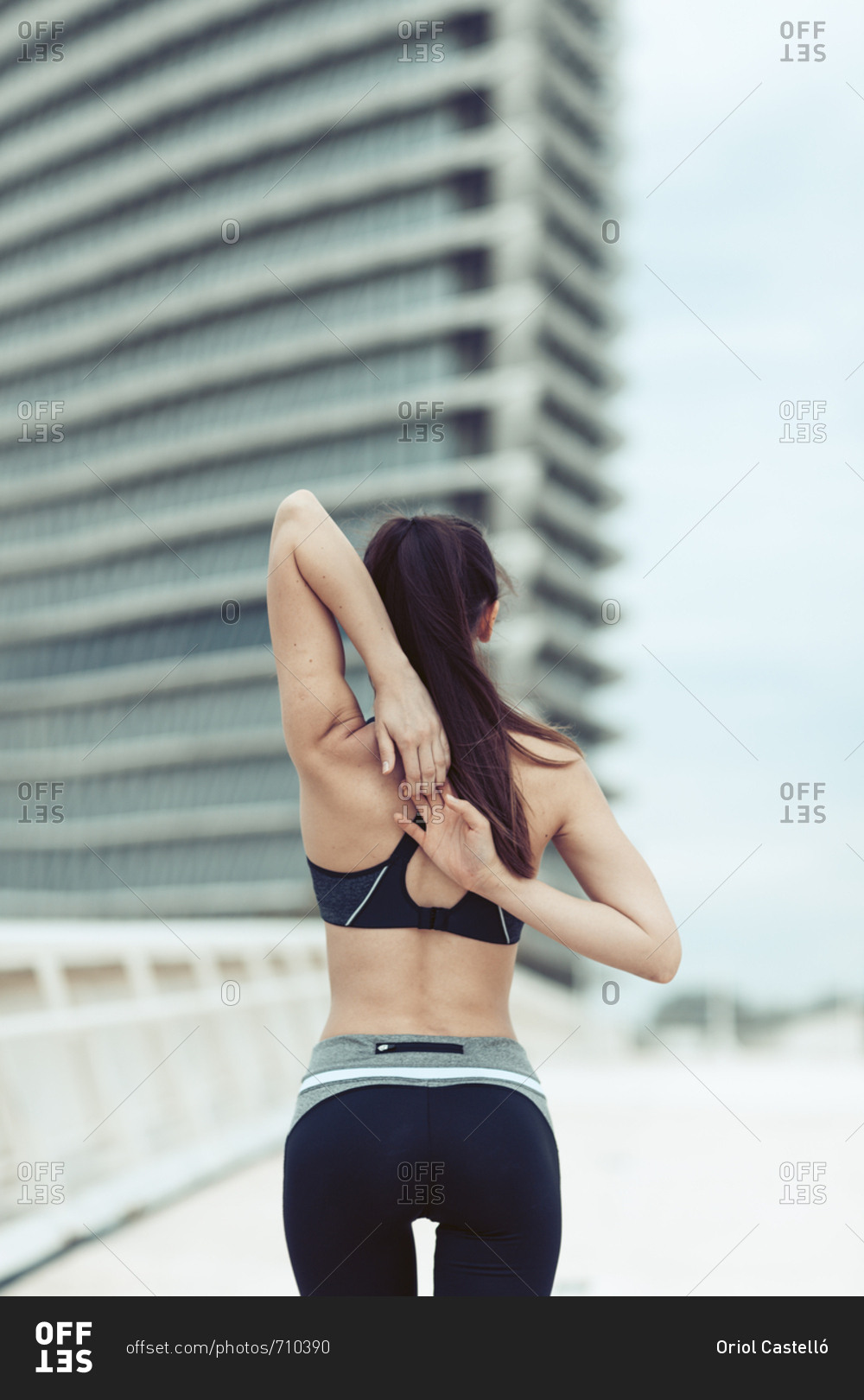 Rearview of athletic woman in sportswear linking fingers behind back