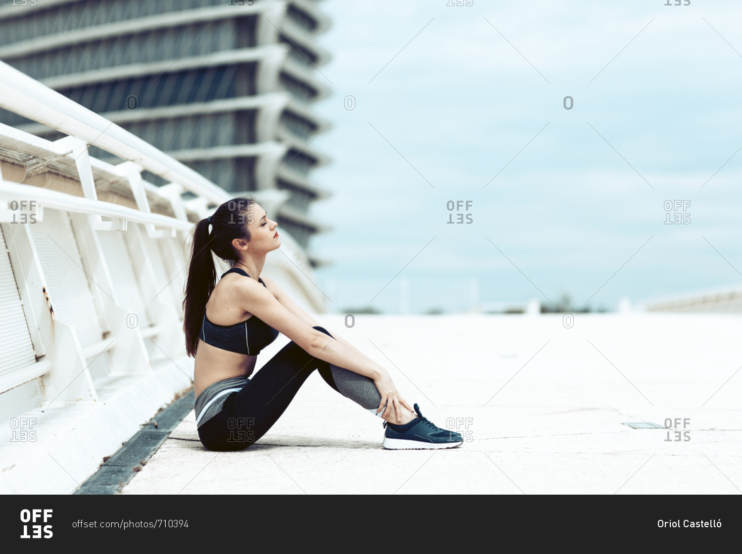 Young woman in sports wear sitting on bridge taking break during workout