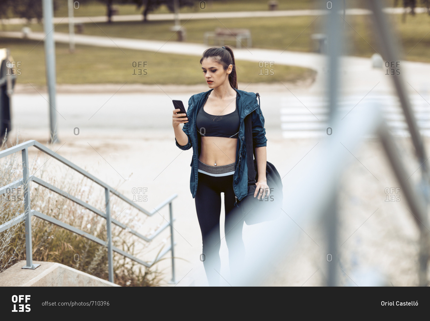 Young woman in sportswear carrying bag pauses to check phone after workout