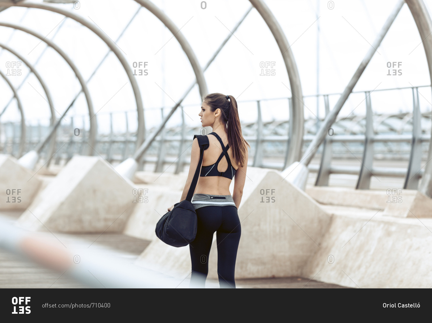 Rearview of woman in athletic wear carrying gym bag walking along bridge