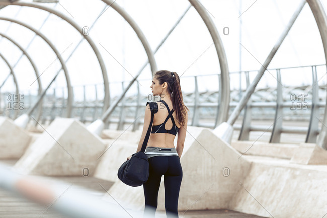 Rearview of woman in athletic wear carrying gym bag walking along bridge