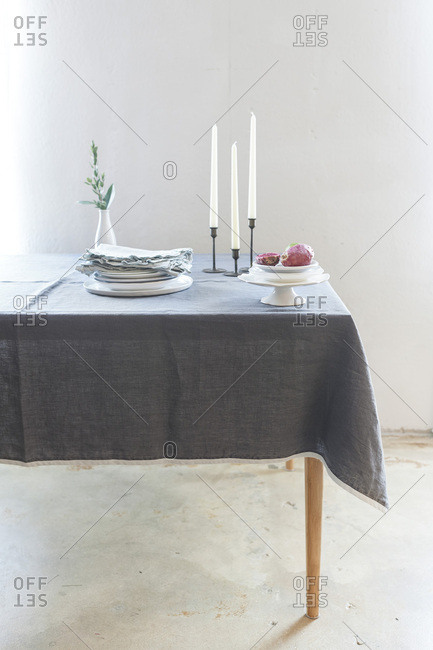 A dinner table with a gray linen table cloth set with white plates, blue table linens and candles.