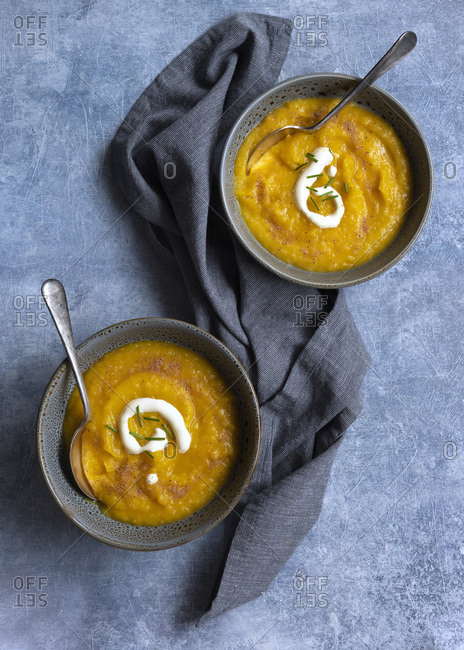 Two bowls of thick pumpkin soup with spoons on a blue textured background.