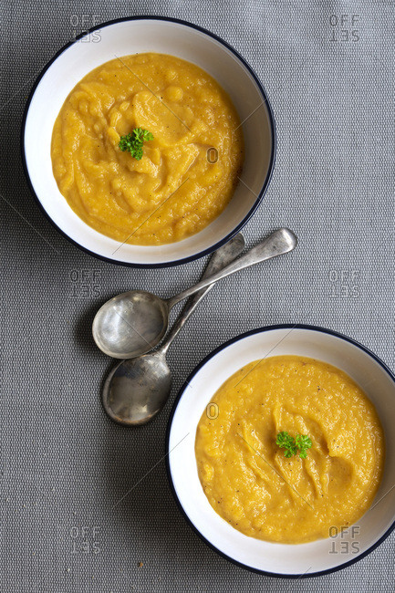Two bowls of homemade pumpkin soup with two spoons.