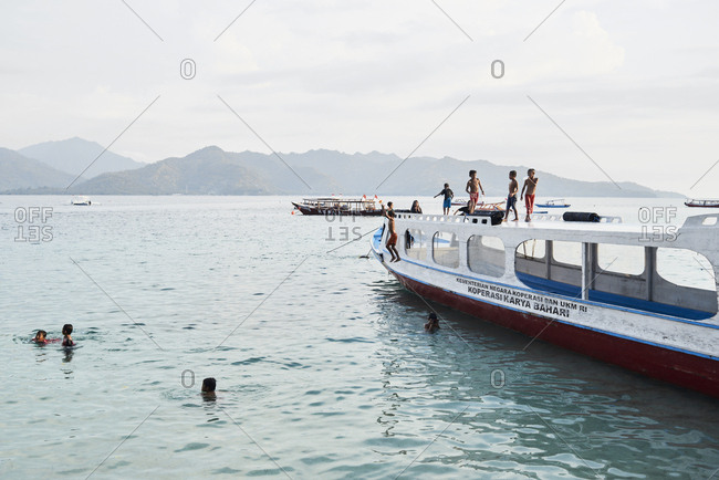 Gili Islands, Indonesia - April 11, 2018: bunch of local indonesian boys running and jumping into water from the top of a moored boat at sunset.