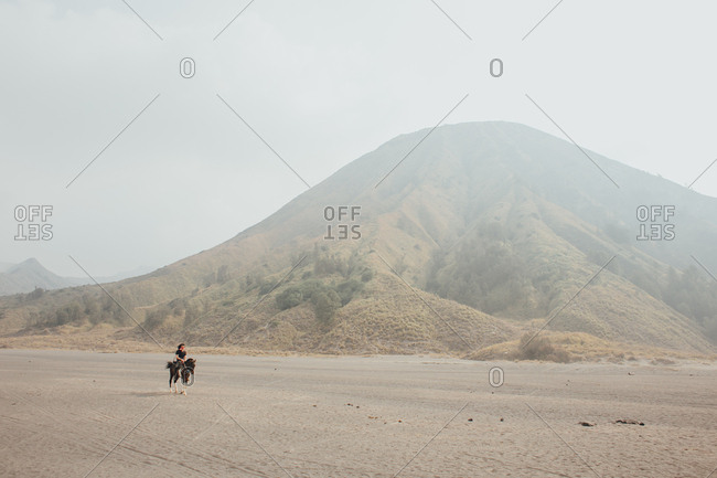 Single rider on horseback travelling through barren sandy terrain with hills in background