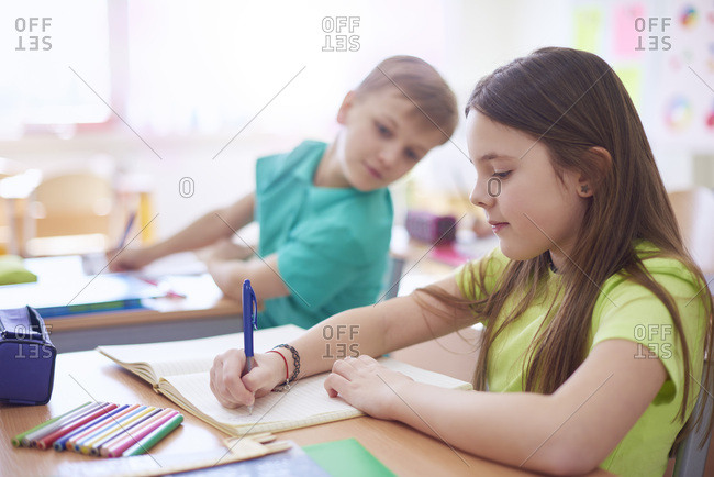 Schoolboy looking at schoolgirl writing in exercise book in class