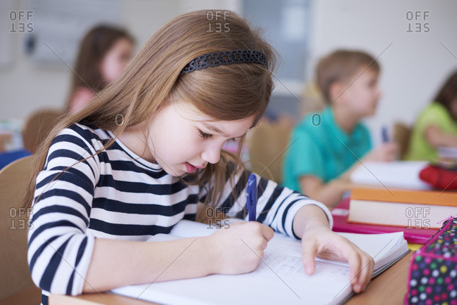 Schoolgirl writing in exercise book in class