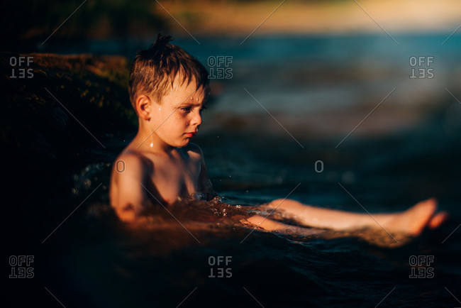 Unhappy young boy sitting in water bathed in afternoon light