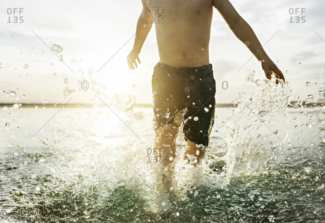 Cropped view of boy running through shallow water at sunset