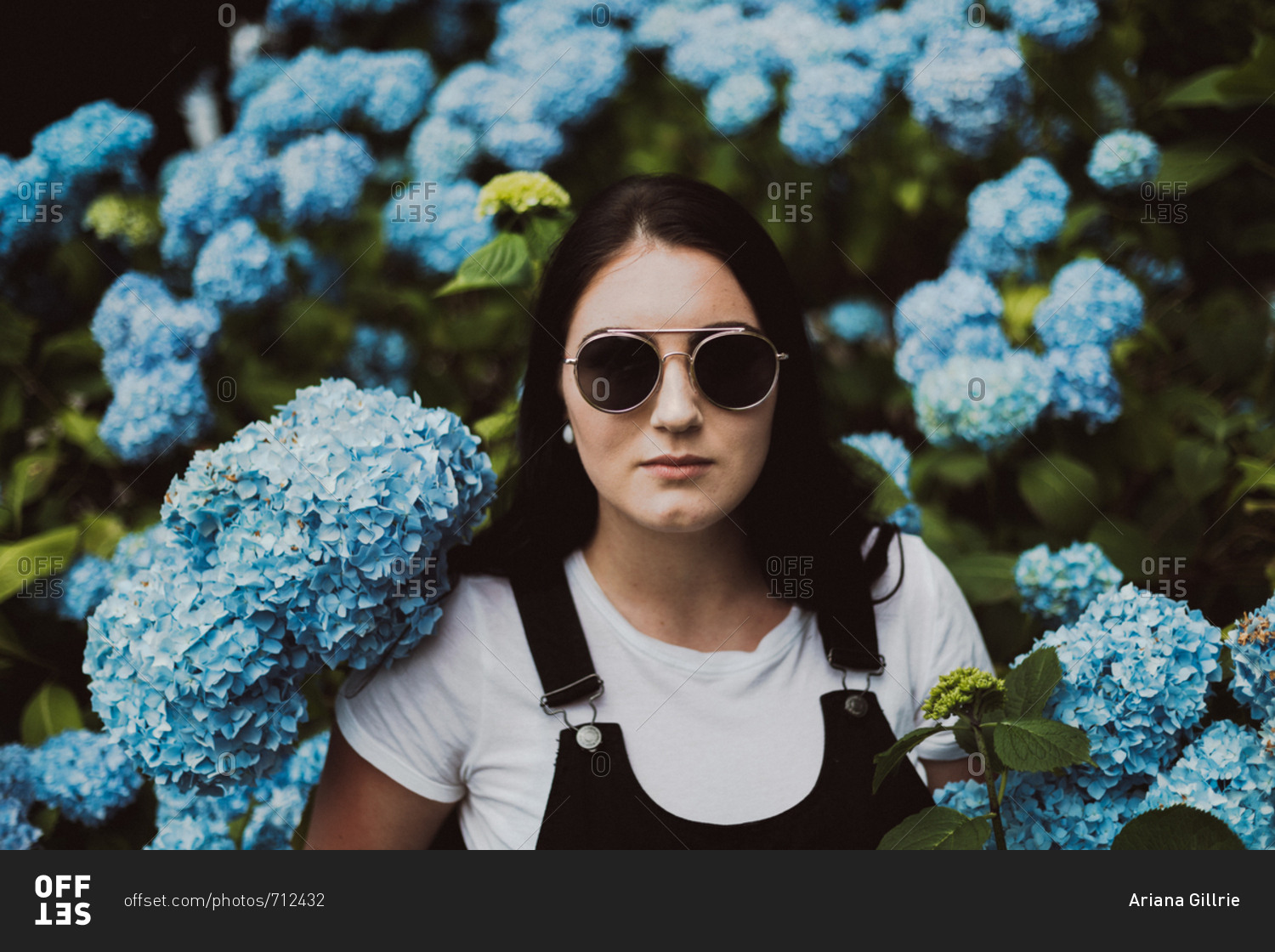 Portrait of a young woman wearing sunglasses standing among blooming hydrangeas