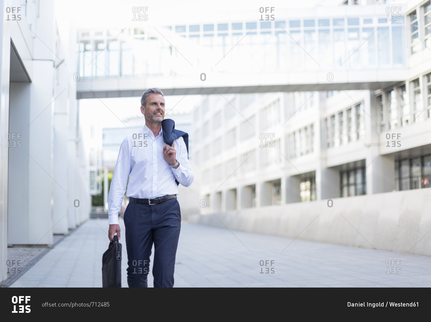 Businessman with laptop bag walking at courtyard of modern office buildings