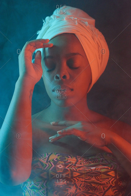 Waist-up portrait of young pretty African American woman wearing head wrap and swimsuit posing in the dark with her eyes closed